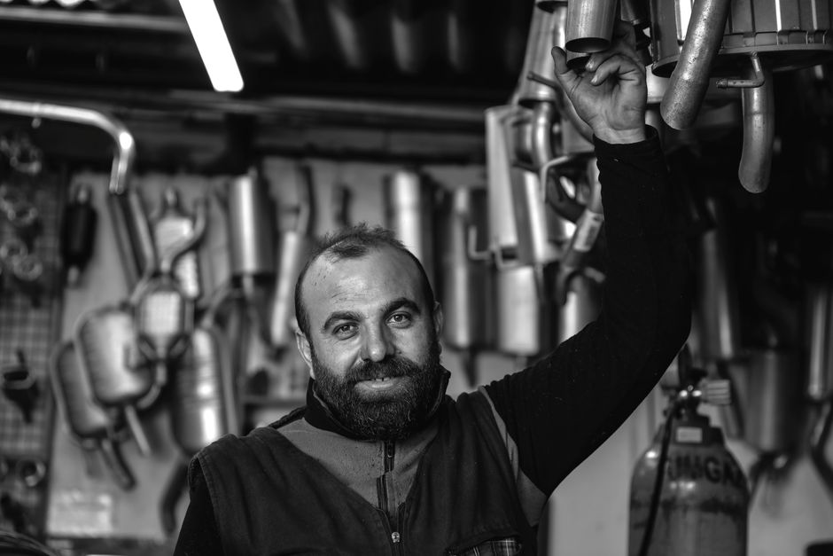 A smiling mechanic holding an exhaust pipe in a car repair garage. Black and white photo.